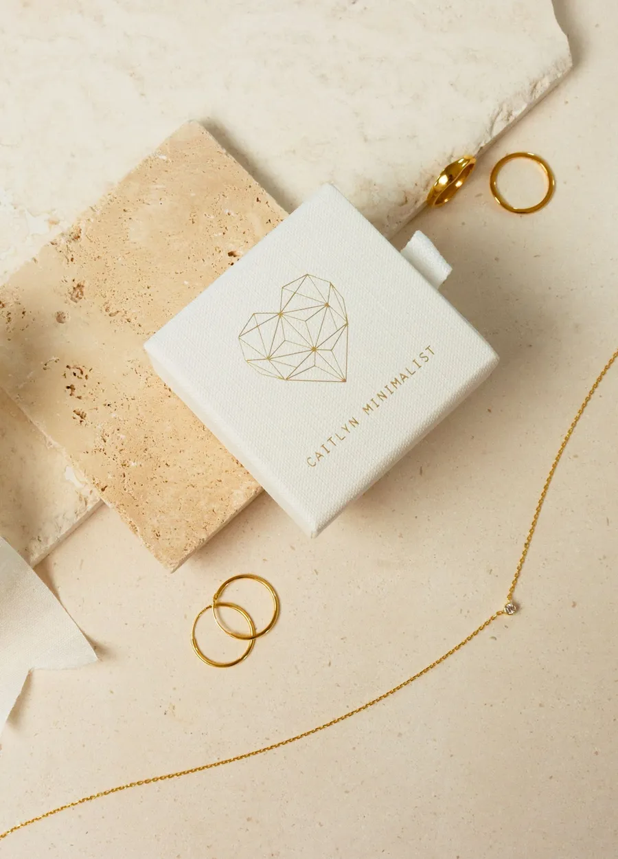 The gift box on travertine with gold hoops, a ring and a fine chain laid around it