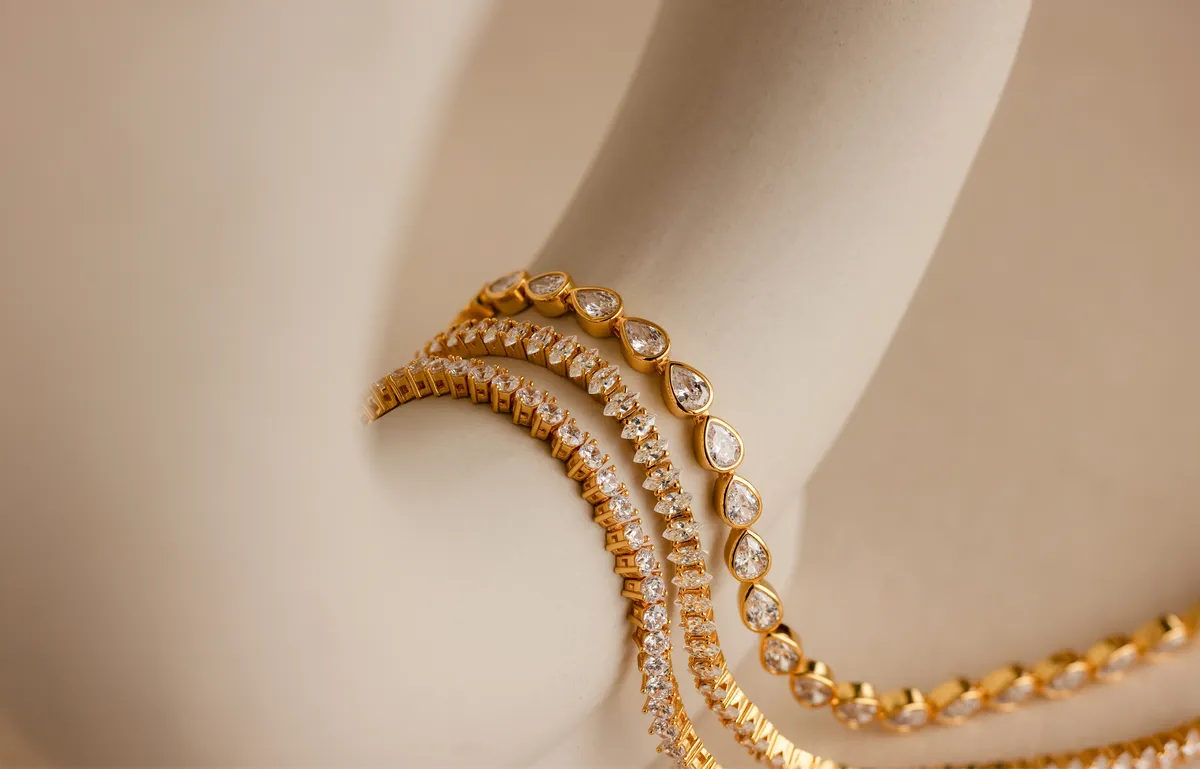 Gold beaded bracelets draped over a pale ceramic form