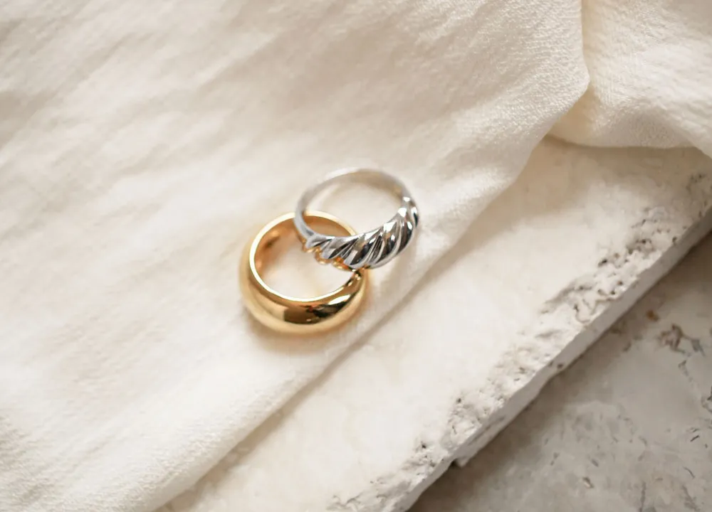 A gold dome ring and a silver croissant ring on white linen