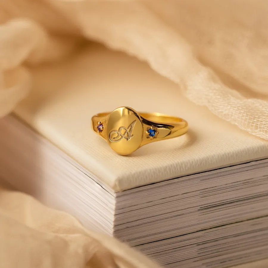 Initial Birthstone Signet Ring engraved with a script A, resting on a stack of paper