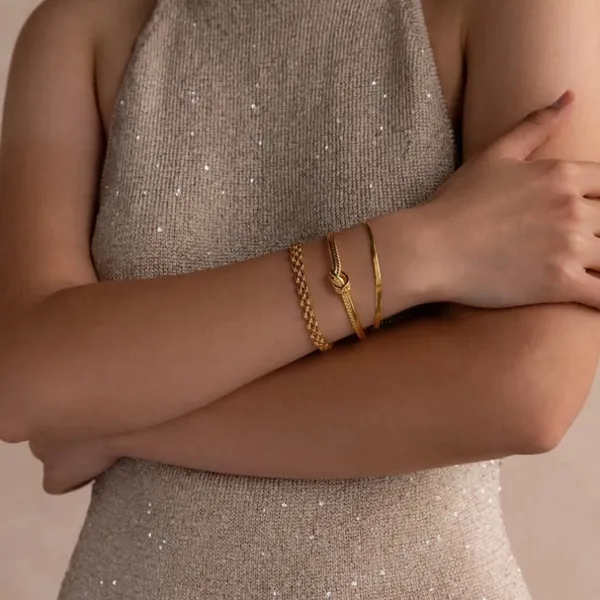 Crossed arms wearing gold bracelets over a sequined dress