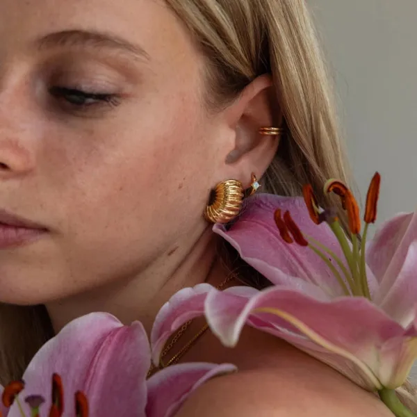 A woman wearing gold earrings beside pink lilies