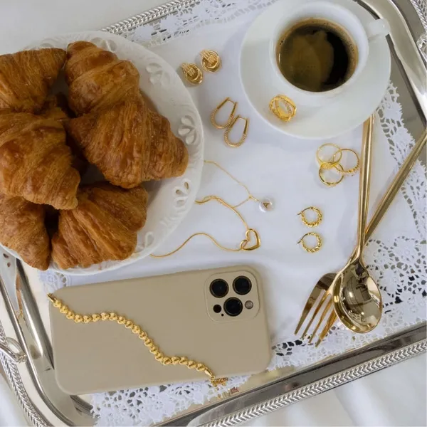 Gold jewelry laid out on a breakfast tray with croissants and coffee