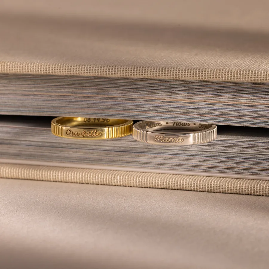 A gold Ribbed Name Ring and a silver engraved ring on the edge of a beige book