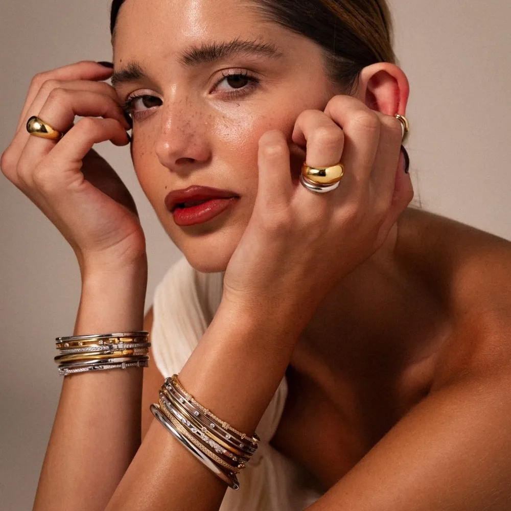 A woman resting her face in her hands, wearing stacked rings and bangles