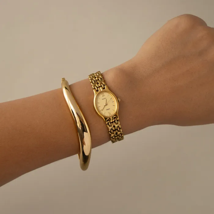 Vintage Seiko Belfina Oval Woven Gold Watch on a wrist beside a gold bangle